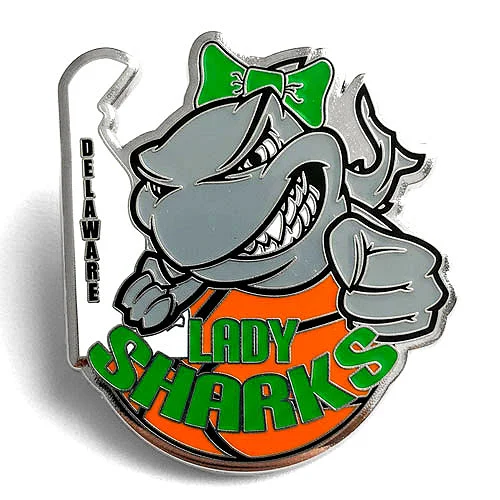 Custom trading pin featuring a fierce gray shark with a green bow, clenching a fist over an orange basketball. The words “Lady Sharks” appear in bold green and black text, with “Delaware” written vertically along the left edge.