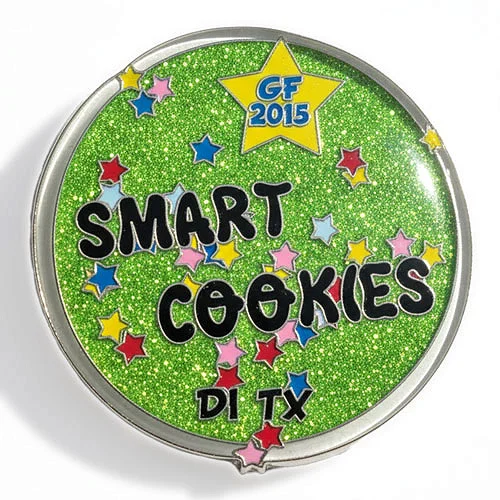 Smart Cookies 2015 custom trading pin from Texas DI with glitter and star design. Round custom trading pin with a bright green glitter background and multicolored stars scattered across the surface. Bold black text reads “Smart Cookies,” with “DI TX” at the bottom and a yellow star at the top labeled “GF 2015,” representing a Texas Destination Imagination team.