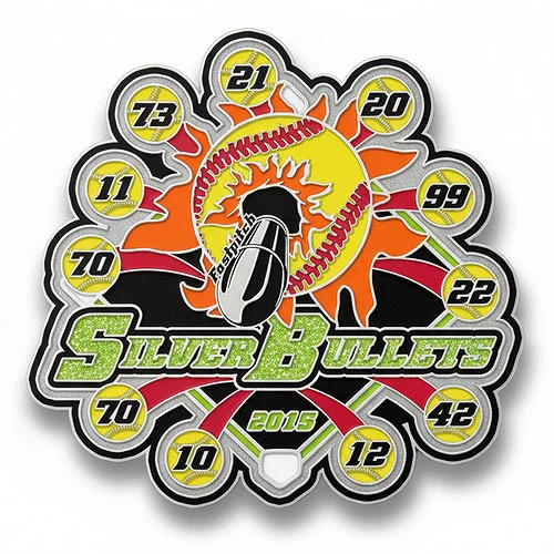 Custom trading pin for the Silver Bullets 2015 softball team, featuring a large silver bullet over a fiery yellow and orange softball with red stitching. The glittery green team name is centered, with player numbers in yellow softballs circling the design.